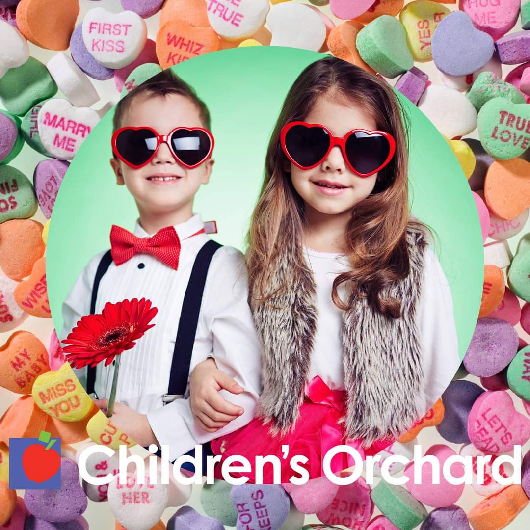 Two kids wearing heart shape sunglasses surrounded by candy hearts.
