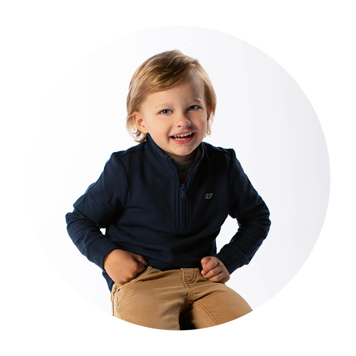 Toddler boy sitting on a chair wearing a navy vineyard vines sweater and khaki pants,