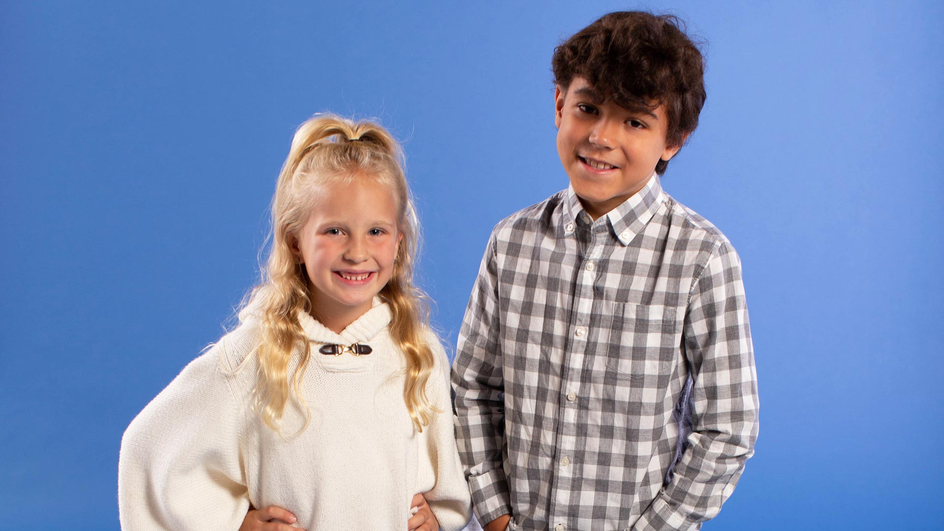 Elementary aged girl wearing a white sweater standing next to an elementary aged boy wearing a flannel shirt.